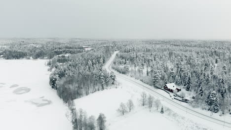 Aerial,-rising,-drone-shot,-of-a-slippy-road,-between-snow,-covered-trees-and-winter-forest,-on-a-overcast-day,-near-Nuuksio-national-park,-in-Espoo,-Uusimaa,-Finland
