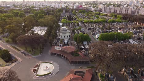 Aerial-flyover-church-of-Chacarita-Cemetery-during-sunset-in-Buenos-Aires-City---Beautiful-cityscape-skyline-in-background