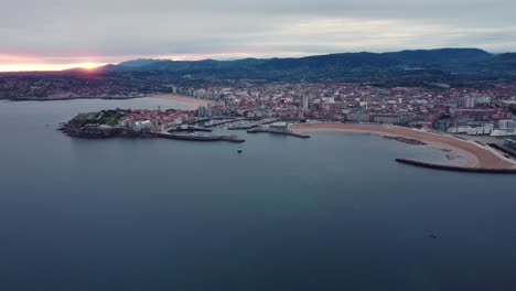 Drone-Vuela-Sobre-La-Ciudad-De-Gijón-Al-Norte-De-España-Región-De-Asturia,-Puesta-De-Sol-Paisaje-Urbano-Vista-Al-Mar