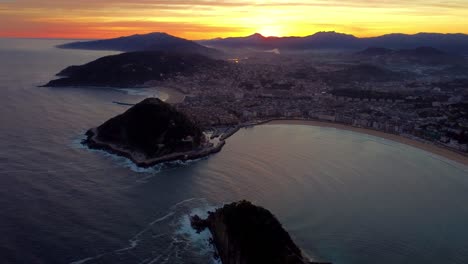 Aerial-footage-San-Sebastián-cityscape-during-epic-morning-sunrise-colourful-sky-behind-the-mountain