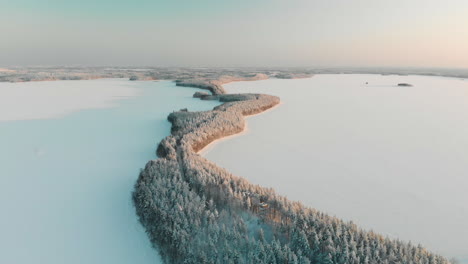 Aerial,-tracking,-drone-shot,-panning-above-Vuoniemi-ness,-in-the-middle-of-snowy-lake-Saimaa,-full-of-pine-tree-forest,-at-sunset,-on-a-sunny,-winter-evening-dusk,-in-North-Karelia,-Finland