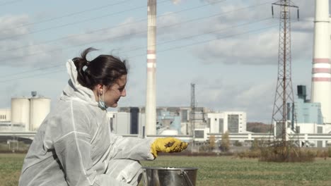 Laboratory-worker-is-soil-sampling-field-with-power-factory-in-background