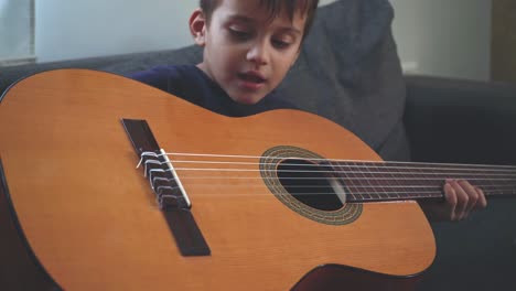 Caucasian-four-years-old-boy,-tying-to-play-a-classic-guitar-at-home-4K,-close-up-30fps
