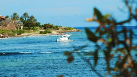 White-fishing-boat-sailing-to-shore-in-colorful-Caribbean-landscape,-SLOWMO