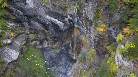 Cascada-En-El-Paisaje-Paradisíaco-Con-Colores-Otoñales-Y-Hermosas-Rocas,-Ovejas-Pastan-En-Pradera-Alpina