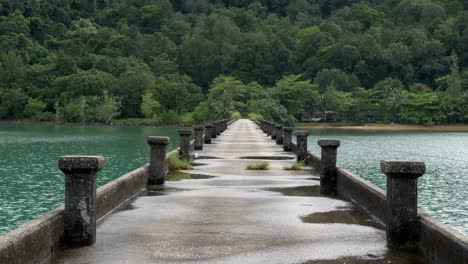 Static-shot-of-a-concrete-pier-in-the-ocean-after-rainfall-with-green-lush-forest-in-the-back
