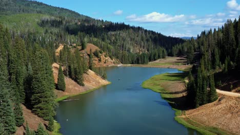 Beautiful-lowering-aerial-drone-shot-of-a-stunning-nature-landscape-of-the-Anderson-Meadow-Reservoir-lake-up-Beaver-Canyon-in-Utah-with-large-pine-tree-forest,-a-small-stream,-and-a-grass-field