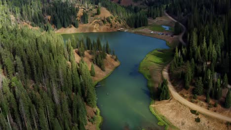 Beautiful-tilting-down-aerial-drone-shot-of-a-stunning-nature-landscape-of-the-Anderson-Meadow-Reservoir-lake-up-Beaver-Canyon-in-Utah-with-large-pine-tree-forest-and-a-parking-lot-for-fisherman