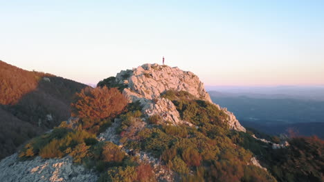 Zoom-In-drone-shot-of-a-woman-doing-yoga-on-top-of-a-mountain-with-the-first-lights-of-sunrise