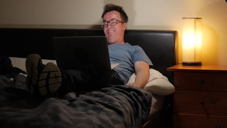 Man-laying-upright-in-bed-gets-excited-watching-sport-on-his-laptop