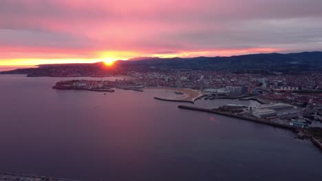 Luftaufnahme-Des-Sonnenaufgangs-Der-Stadt-Gijón-In-Spanien,-Drohne-Fliegt-über-Dem-Hafen-Und-Dem-Strand