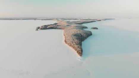 Aerial,-reverse,-drone-shot,-of-Vuoniemi-cape,-in-the-middle-of-snowy-lake-Saimaa,-full-of-pine-tree-forest,-at-sunset,-on-a-sunny,-winter-evening-dusk,-in-North-Karelia,-Finland