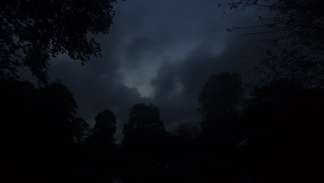 Dunkelgraue-Wolken,-Die-Sich-Bei-Einem-Dramatischen-Sonnenuntergang-Im-Herbst-über-Bäume-In-Der-Silhouette-Bewegen