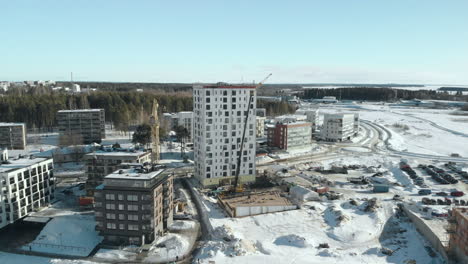 Aerial,-drone-shot,-towards-a-construction-area,-cranes-building-a-apartment-house,-on-a-sunny,-winter-day,-at-Pielisjoki-in-Joensuu,-Pohjois-Karjala,-Finland