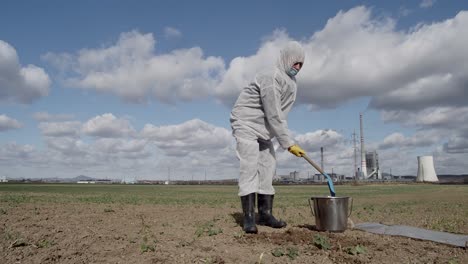 Laboratory-assistant-in-protective-workwear-digging-ground-with-shovel-and-bucket-for-soil-sampling