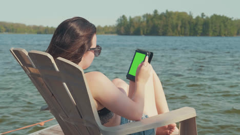 Die-Kamera-Schwenkt-über-Eine-Frau,-Die-Sich-In-Der-Sommersaison-Auf-Einem-Dock-Neben-Einem-See-Entspannt,-Mit-Grünem-Bildschirm-Für-Chroma-Key