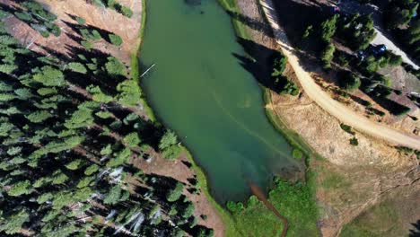 Beautiful-aerial-drone-top-bird's-eye-spinning-shot-of-a-small-stream-surrounded-by-a-field-of-grass-that-leads-into-the-Anderson-Meadow-Reservoir-lake-up-Beaver-Canyon-in-Utah-on-a-warm-summer-day