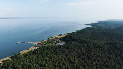 Juodkrante-town-with-small-pier-surrounded-by-dense-forest-and-Curonian-lagoon,-aerial-drone-view