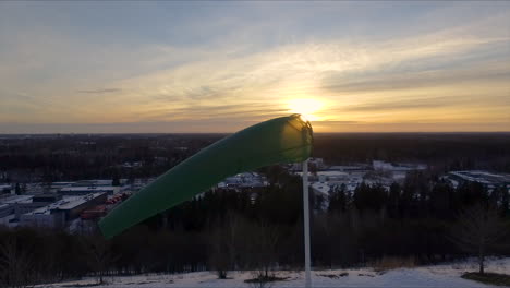 Close-up-aerial-shot-of-a-windsock-billowing-in-a-steady-breeze-on-a-crisp-early-morning-with-the-sun-slowly-rising-in-the-background