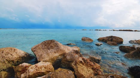 SLOWMO-water-lapping-ocean-rocks,-heavy-storm-clouds-in-background,-Caribbean