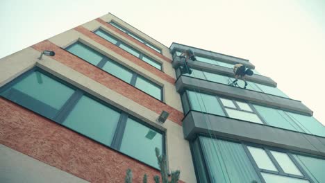 Looking-up-to-high-altitude-climber-alpinists-cleaning-windows-on-high-office-building