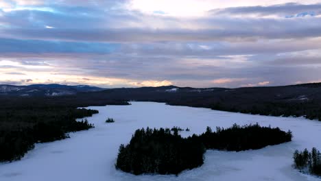 Aerial-footage-flying-backwards-away-from-a-pine-covered-island-in-the-middle-of-a-frozen-lake-at-sunset