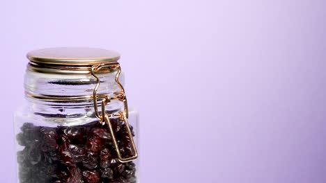 Close-up-of-an-airtight-mason-jar-rotating-with-dehydrated-cranberry-on-a-neon-lilac-background
