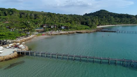 Aerial,-pan,-drone-shot-of-a-wooden-pier-and-building,-at-a-paradise-beach,-on-a-sunny-day,-in-Koh-Kood,-Thailand,-Asia