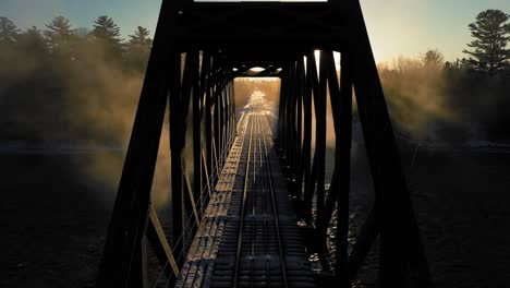 Aerial-CRANE-UP-of-a-backlit-railroad-trestle-with-the-winter-sunrise-blinking-in-an-out-though-the-cribwork-of-the-trestle