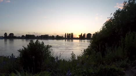Timelapse-on-sunset-behid-the-river-and-long-transporting-boat-traffic
