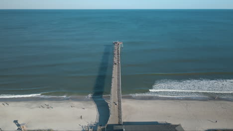 Aerial-shot-flying-over-pier-at-Kure-Beach-waves-lapping-on-shoreline