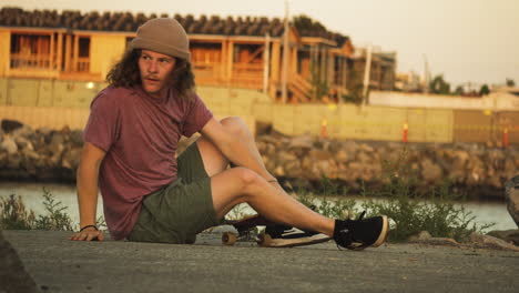 Skateboarder-with-long-curly-hair-gets-up-from-ground,-puts-his-beanie-on-and-rides-away