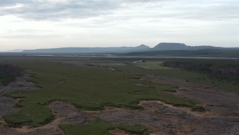 Flying-away-from-Asbyrgi-canyon-above-Eyjan-rock-formation-in-Iceland,-cloudy