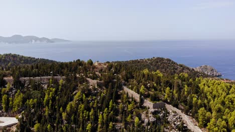 Mountain-Path-Towards-Assos-Castle-In-Asos,-Kefalonia-Greece-On-A-Foggy-Afternoon-By-The-Agia-Kyriaki-Bat--aerial-shot