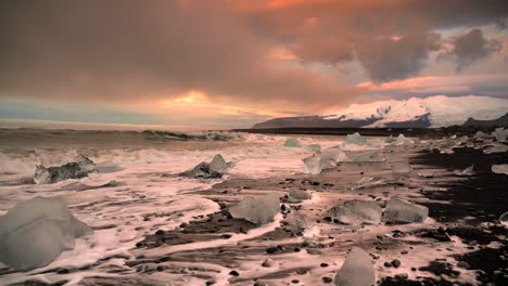 Wide-shot-of-Diamond-Beach-during-mystic-sunrise-in-Iceland---Waves-reaching-shore-with-icebergs-in-slow-motion