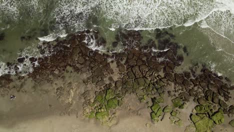Hypnotic-shot-tracking-breaking-waves-on-rocky-beach-shoreline-topdown-aerial