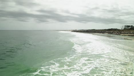Waves-lapping-on-shoreline-of-Kure-Beach-low-aerial-shot