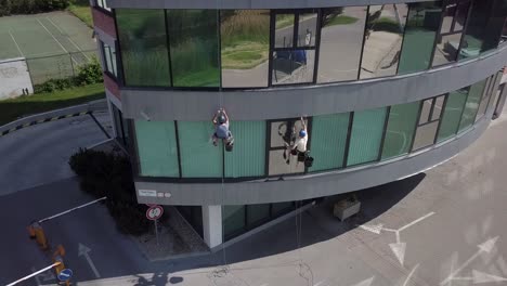 Descending-rotating-aerial-across-high-altitude-climber-workers-cleaning-office-windows