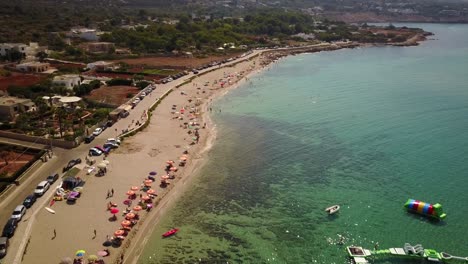 View-from-the-sky-of-a-beach-by-the-Mediterranean-Sea,-full-of-people-lounging