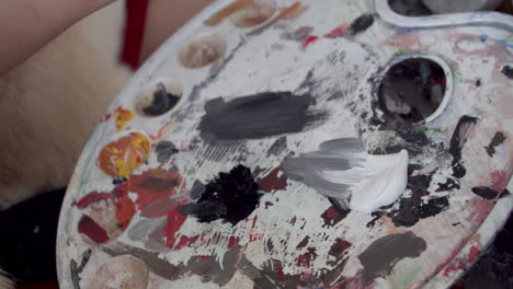 Hand-of-artist-mixing-paint-on-white-color-palette,-close-up-view