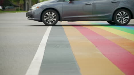 Autos-Fahren-In-Zeitlupe-über-Einen-Regenbogen-zebrastreifen-Mit-Rollerbladern-Im-Hintergrund