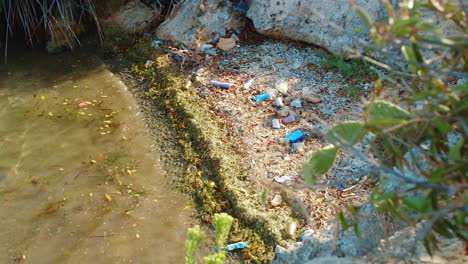 Aerial-reveal-of-plastic-bottles-and-litter-washed-up-on-beach-alcove,-sunny-day