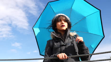 Young-woman-with-blue-umbrella-and-sky-preparing-for-a-rain-storm-to-come-through-after-she-checked-the-weather-SLOW-MOTION
