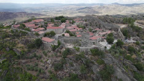 Vista-Orbital-Aldea-De-Casas-De-Piedra-Dentro-De-Muros-De-Fortificación,-En-La-Cima-De-Una-Colina-Verde,-Sortelha