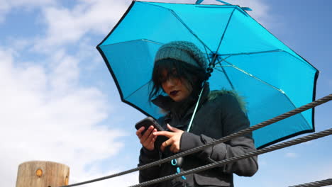 Junge-Frau,-Die-Das-Wetter-überprüft-Oder-Auf-Dem-Smartphone-Mit-Regenschirm-Unter-Blauem-Himmel-Mit-Regenwolken-Zeitlupe-Simst