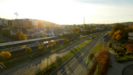 Taking-off-over-Gdynia-Redlowo-railway-station-and-droga-Gdynska-highway-early-in-the-morning-at-bright-Autumn-sunrise---aerial-view,-car-moving-on-expressway