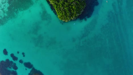 Cinematic-drone-shot-of-a-blue-lagoon-revealing-a-small-island-rock-formation-near-the-beach-in-a-tropical-area-during-the-day