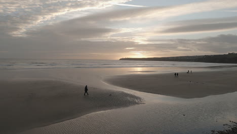 People-walk-dogs-on-wide-sandy-Irish-Atlantic-beach-in-early-evening