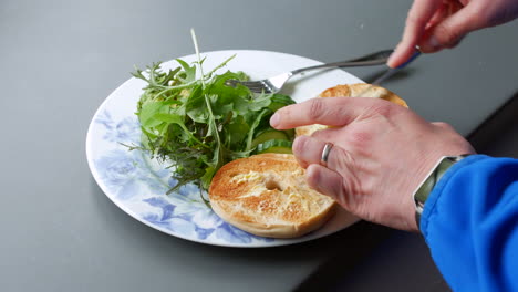 Woman-buttering-a-bagel-and-salad-for-breakfast