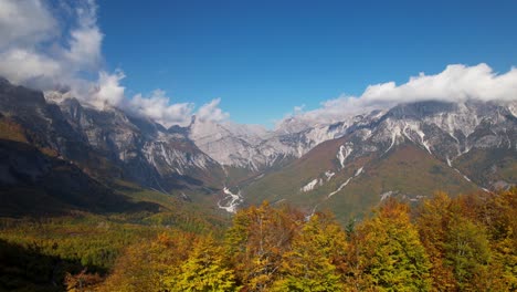 Autumn-landscape-with-golden-leaves-of-trees-and-Alpine-mountain-background,-clouds-and-blue-sky
